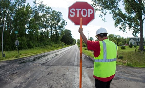 Man in yellow construction vest holding stop sign in middle of road